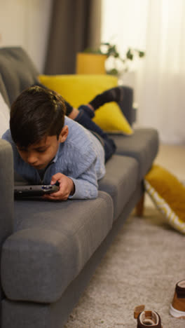 Video-Vertical-De-Un-Niño-Acostado-En-Un-Sofá-En-Casa-Jugando-O-Transmitiendo-A-Un-Dispositivo-De-Juegos-Portátil-1